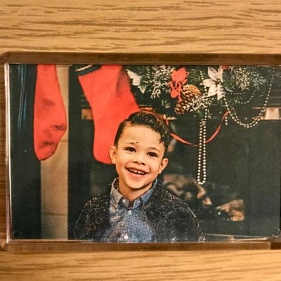 Fotografia de menino sorridente em moldura acrílica com decoração natalícia ao fundo
