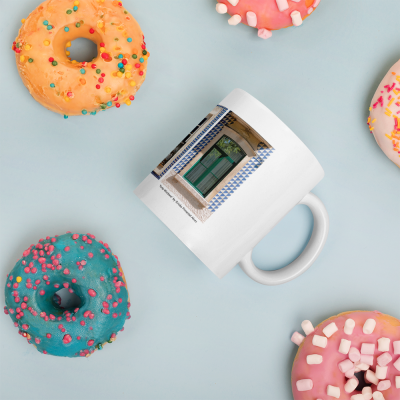Caneca branca com porta verde impressa rodeada por donuts coloridos sobre fundo azul claro