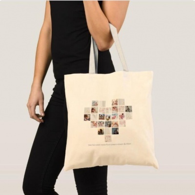 Mala tote bege com padrão de coração formado por quadrados e texto impresso, segurada por pessoa com roupa preta