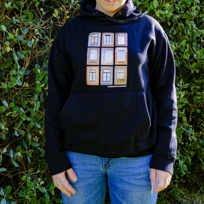 Pessoa a usar casaco com capuz preto e estampa de janelas, fundo de plantas verdes