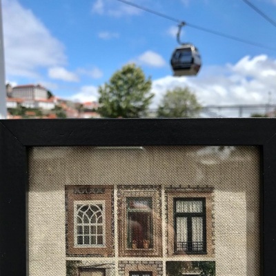 Quadro com impressão de fachada de edifício com janelas e portas, céu azul, árvore e teleférico preto ao fundo