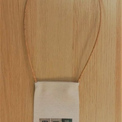 Saco pequeno de tecido com estampa de janelas e alça castanha pendurado numa superfície de madeira