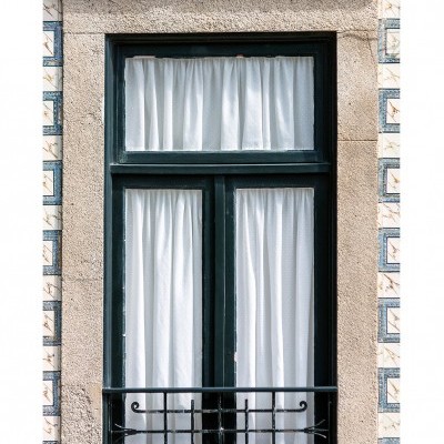 Janela com cortinas brancas e moldura verde escuro num prédio com azulejos azuis e brancos