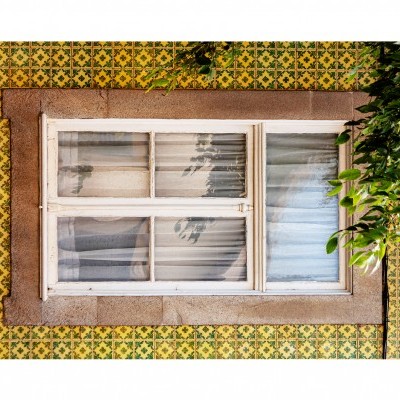 Janela branca com cortinas em parede de azulejos amarelos com padrão verde e moldura de pedra rosa