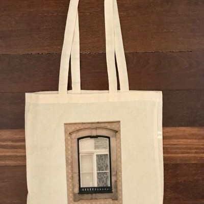 Saco de tecido bege com imagem de janela impressa, sobre mesa de madeira.