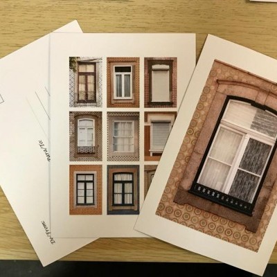 Postais com imagens de janelas de vários estilos sobre mesa de madeira clara