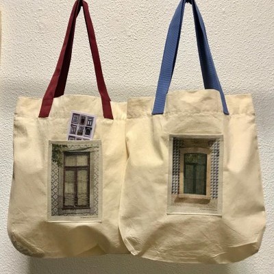 Duas sacolas creme com imagens de janelas e alças vermelha e azul