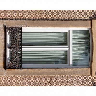 Janela com moldura branca, cortinas verdes e guarda-corpo em ferro forjado preto numa parede com azulejos geométricos vermelhos e brancos