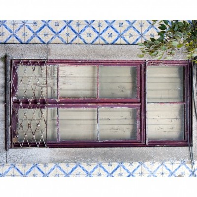 Janela de madeira vermelha com rede metálica numa parede de azulejos azuis e brancos