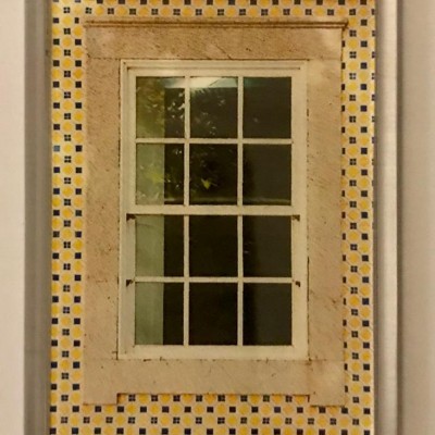 Imã com imagem de janela branca emoldurada por azulejos amarelos e azuis com texto na base