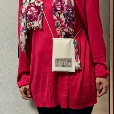 Pessoa com camisa vermelha, cachecol floral e bolsa creme com impressão de janelas.