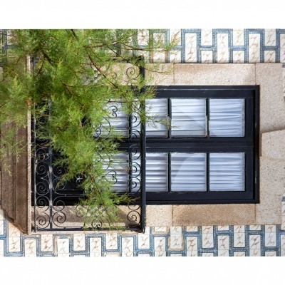 Janela preta com grades de ferro em fachada de azulejos azuis e brancos com árvore à frente