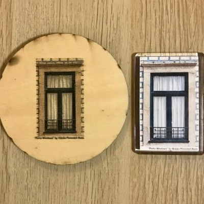 Porta-copos redondo e íman retangular com fotografia de janela preta com cortinas brancas sobre madeira clara