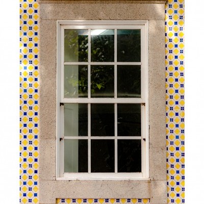 Janela de madeira branca com múltiplos painéis de vidro e moldura de pedra em parede de azulejos coloridos