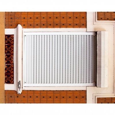 Janela branca com estore e azulejos geométricos no muro amarelo