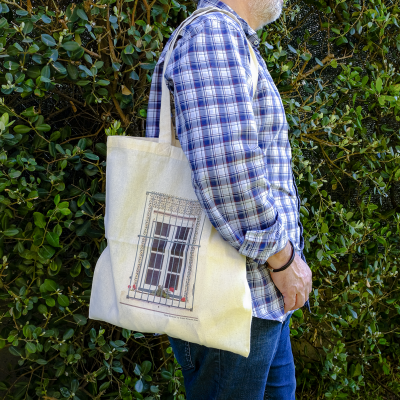 Mala de tecido bege com impressão de janela decorativa em frente a arbusto verde