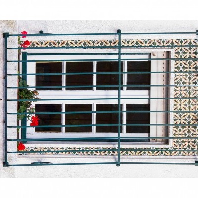 Janela branca com moldura em mármore e azulejos florais, grades verdes e flores vermelhas