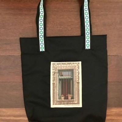 Mala de tecido preta com alças decoradas e imagem de janela com vasos