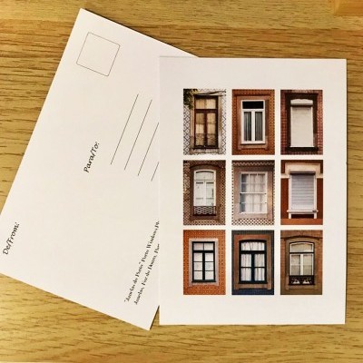 Dois postais com imagens de janelas e espaço para endereço sobre uma mesa de madeira