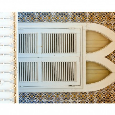 Janela branca de madeira com postigos e moldura em arco, parede com azulejos decorativos