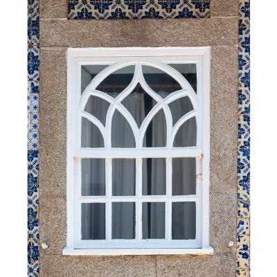 Janela branca com vidro decorativo em parede de pedra rodeada por azulejos azuis e brancos.