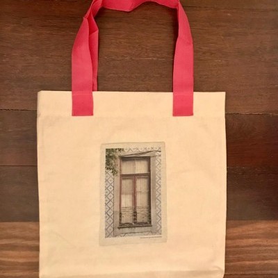 Mala de tecido bege com alças vermelhas e imagem de janela antiga