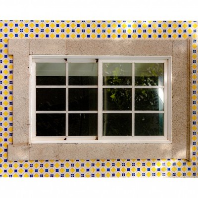 Janela branca em parede de azulejos amarelos, azuis e brancos com moldura de pedra cinzenta