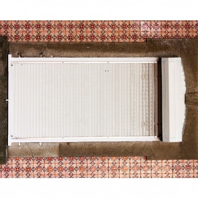 Janela branca com persiana vista de cima, paredes de pedra, piso com azulejos geométricos