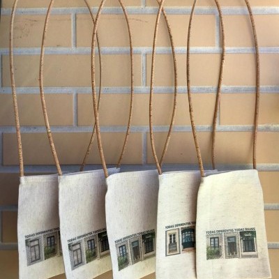 Cinco bolsas pequenas de tecido cru com alças finas de corda penduradas numa parede de tijolos