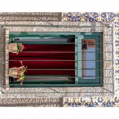 Janela verde com cortina vermelha e plantas em parede de pedra com azulejos