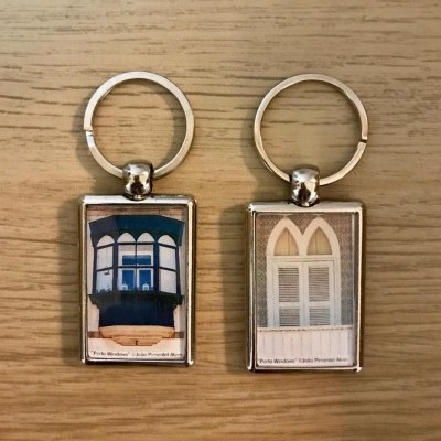 Dois porta-chaves retangulares com imagens de janelas tradicionais, um azul e outro branco, sobre uma superfície de madeira clara