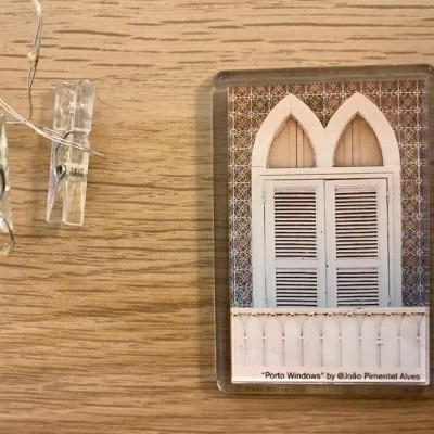 Fotografia em moldura de vidro de uma janela branca com detalhes azulejares sobre uma mesa de madeira clara