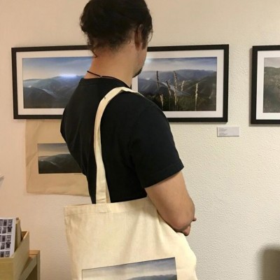 Pessoa de costas com mala de tecido bege com imagem de montanhas.