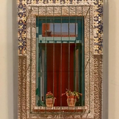 Íman com fotografia de janela em pedra com grelha, moldura verde e plantas em vasos.