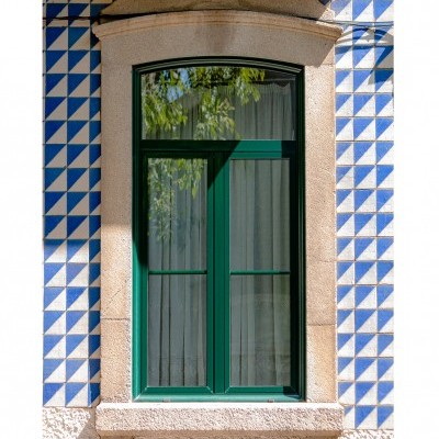 Janela verde escura com moldura de pedra e azulejos azuis e brancos