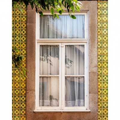 Janela branca com cortinas brancas em parede com azulejos amarelos e verdes