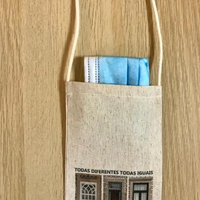 Bolsa de tecido bege com três janelas e texto em português com máscara azul dentro.