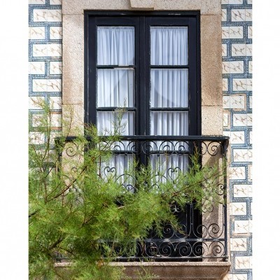 Janela preta de madeira com cortinas brancas, varanda de ferro e azulejos tradicionais azuis e brancos na parede exterior