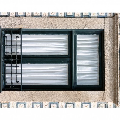 Janela de ferro preto com vidros brancos texturizados e cortinas brancas numa parede azulejada