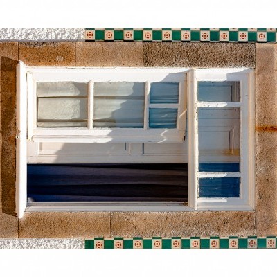 Janela branca com moldura de pedra e azulejos decorativos numa parede branca