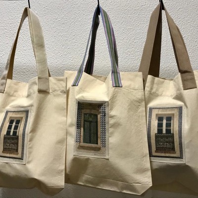 Três sacos de pano bege com imagens de janelas e alças pendurados numa parede branca.