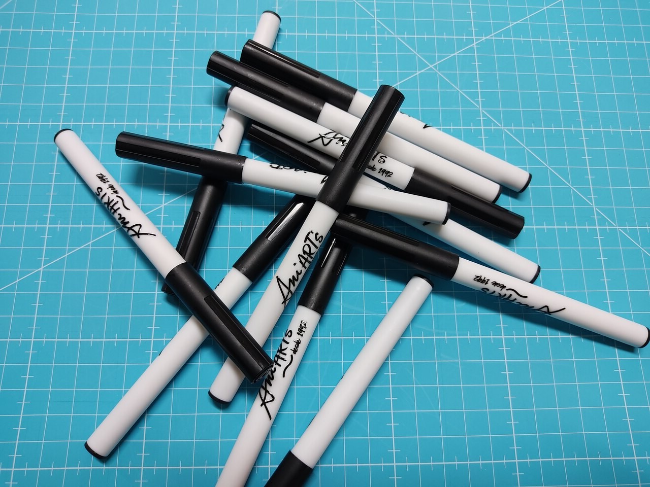 Caneta para transfere Ani Art's LTF01 Marcadores brancos e pretos com texto manuscrito sobre superfície azul quadriculada