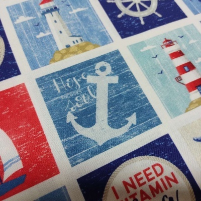 Tecido com padrão náutico em azul, vermelho e branco com faróis, âncoras e texto.