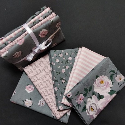 Tecidos decorativos com padrões rosa e cinza, alguns com flores e riscas, pacote amarrado com fita branca