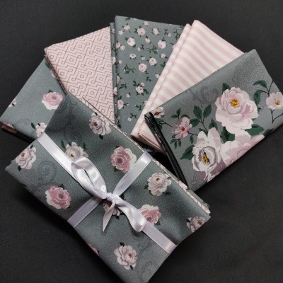 Teares dobrados com padrões florais, geométricos e riscas em tons de cinza, rosa e branco num fundo preto