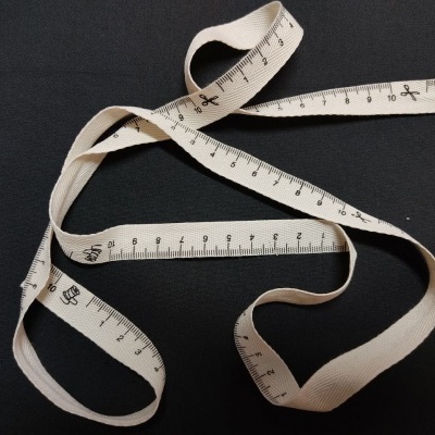 Fita métrica branca de tecido com marcações em preto sobre fundo preto