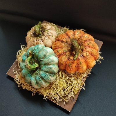 Três abóboras decorativas coloridas sobre base de madeira com palha