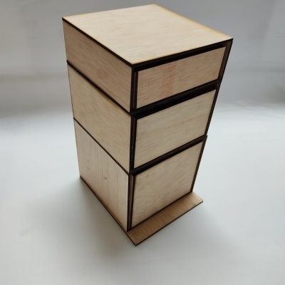 Caixa geométrica de madeira clara com três compartimentos sobre superfície branca