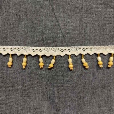 Renda branca com pompons amarelos sobre tecido cinza