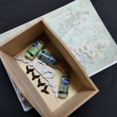 Caixa de madeira com tintas acrílicas e ganchos sobre livro decorado com flores